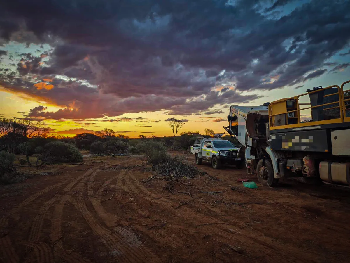 Drill rig and truck silhouetted against a stormy sunset