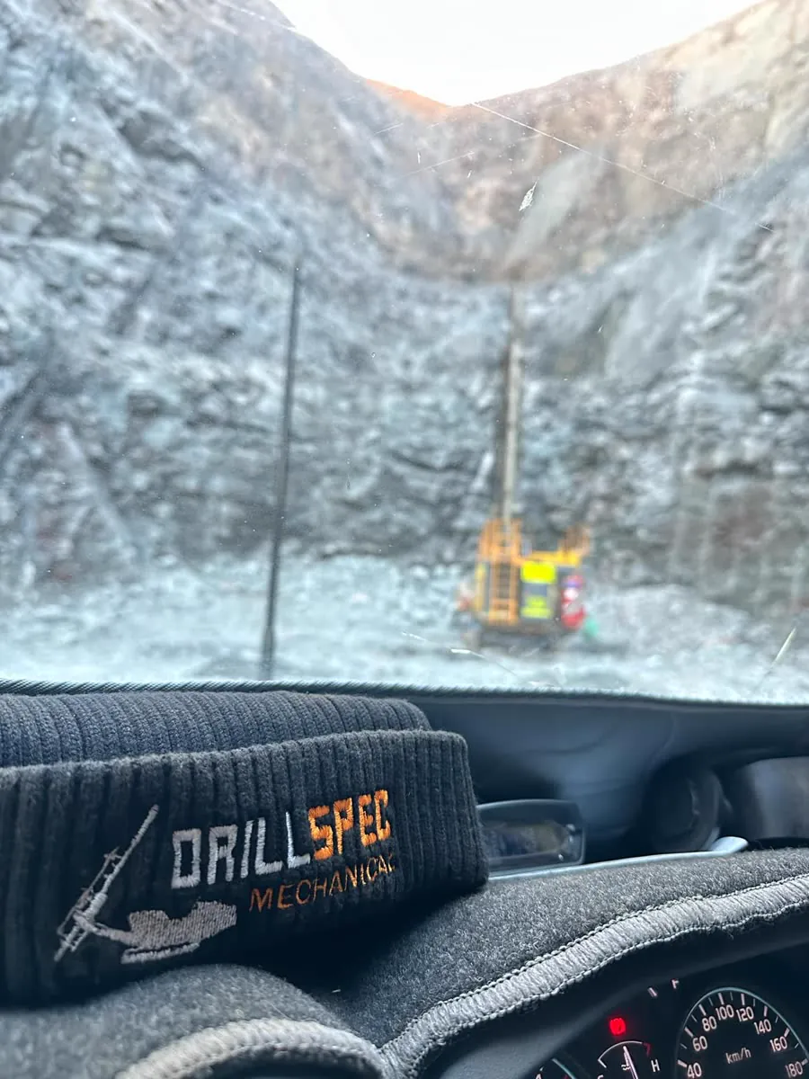 Pit wall and drill rig seen through the ute windscreen, Drillspec beanie on the dash
