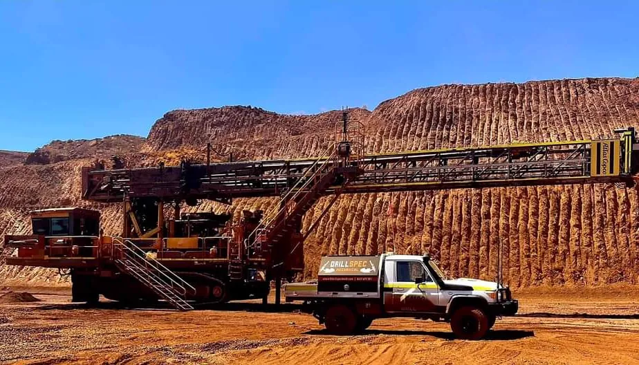 Drillspec service ute beside a tracked surface drill rig under a pit wall