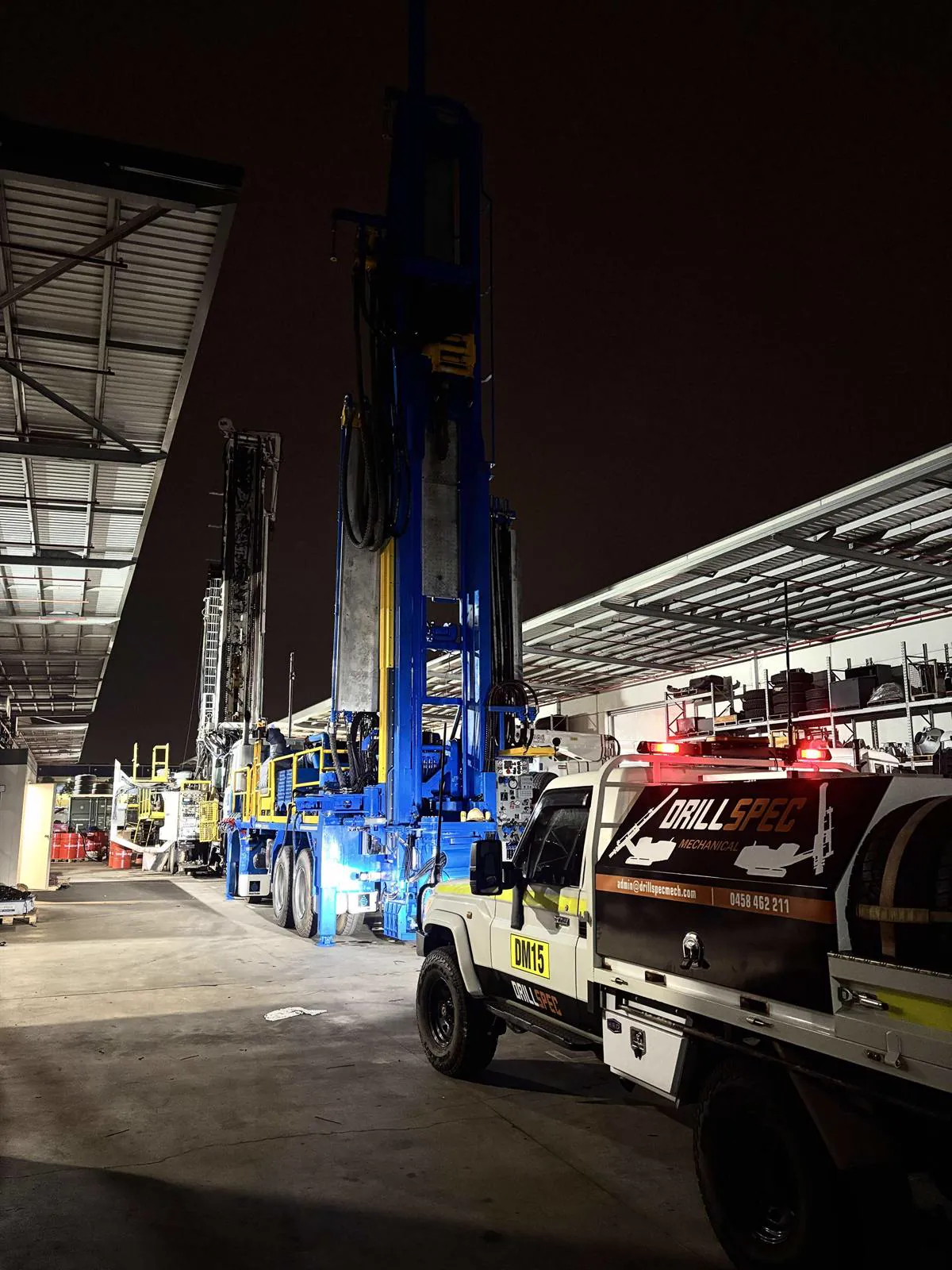 Drillspec DM15 service ute beside a drill rig in the workshop yard at night
