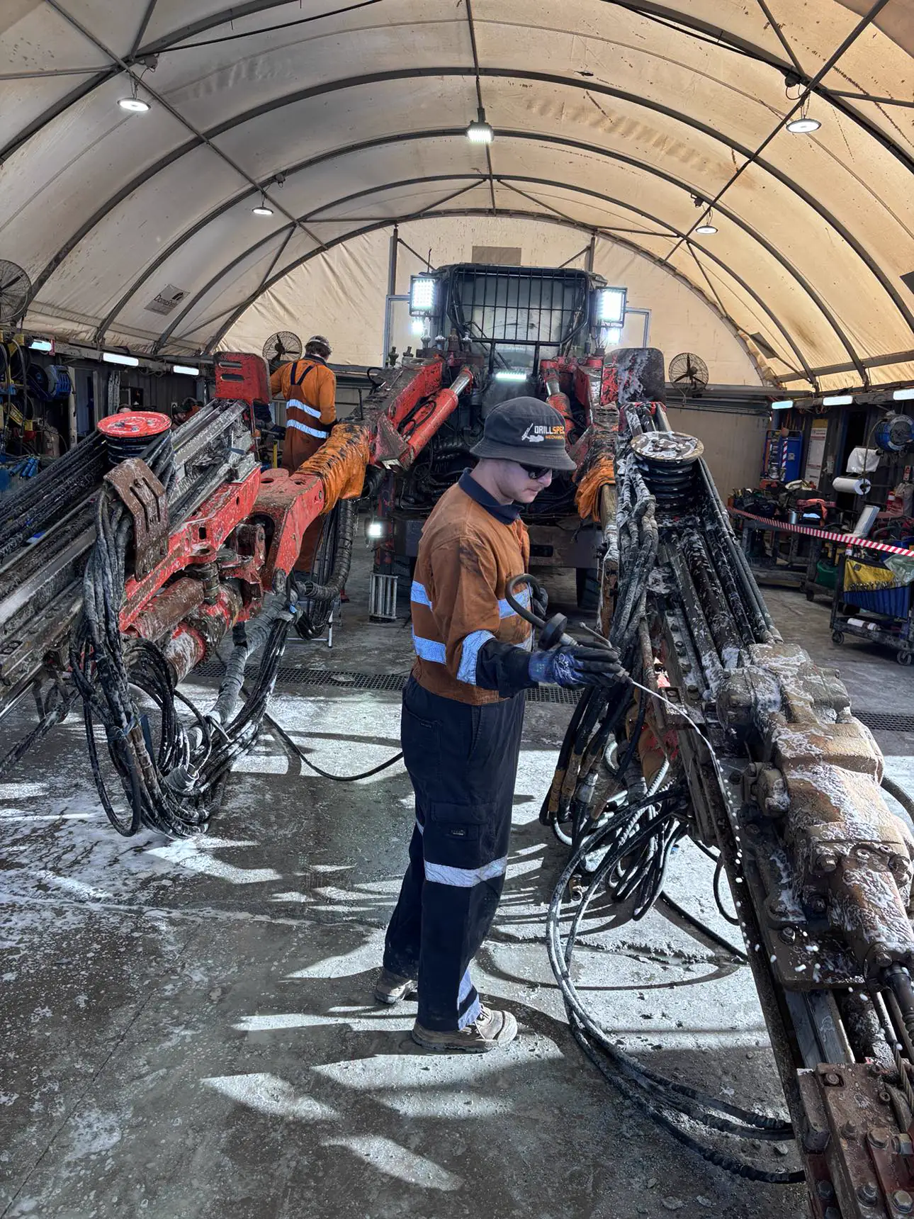 Drillspec technician in branded gear washing down an underground jumbo drill rig in the workshop